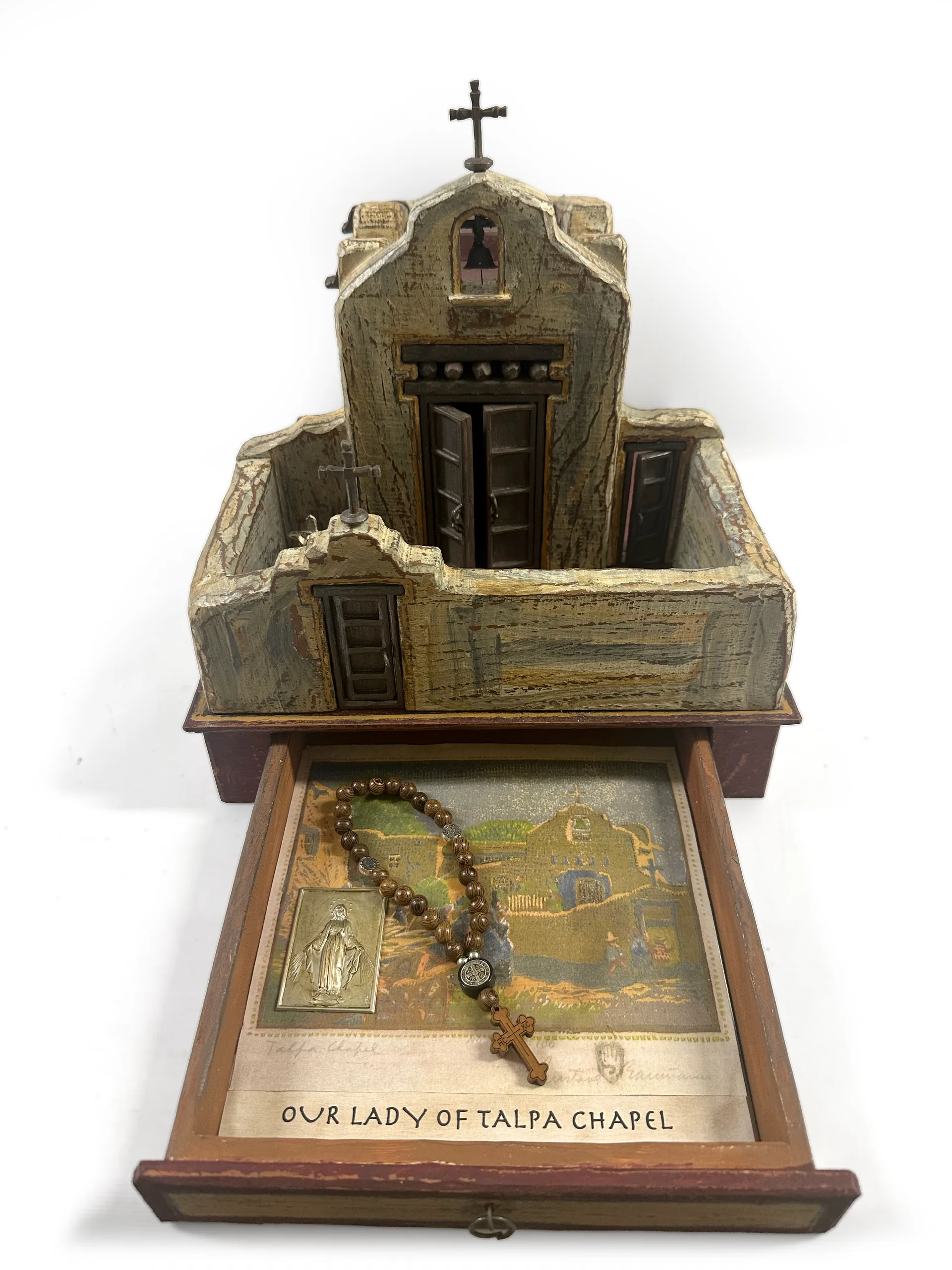 The Talpa Chapel sculpture with the base drawer open, showing PJ Cardinale’s collage of rosaries and devotional cards labelled Our Lady of Talpa Chapel.